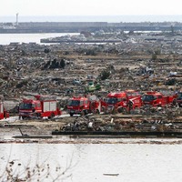 A convoy of emergency vehicles drive past rubble in Natory City on March 13 2011