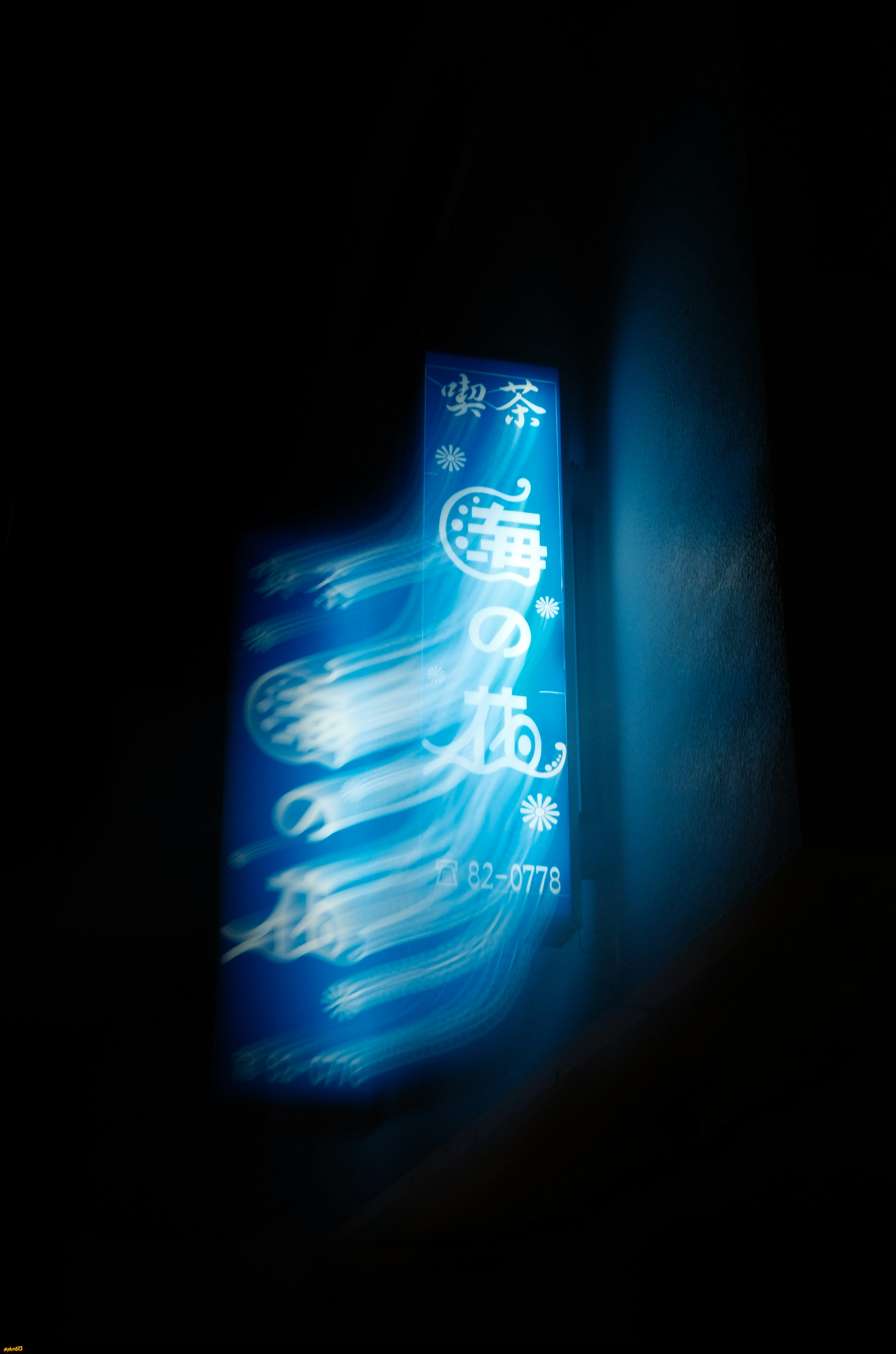 A blurry blue neon sign with japanese characters in darkness by jack berry