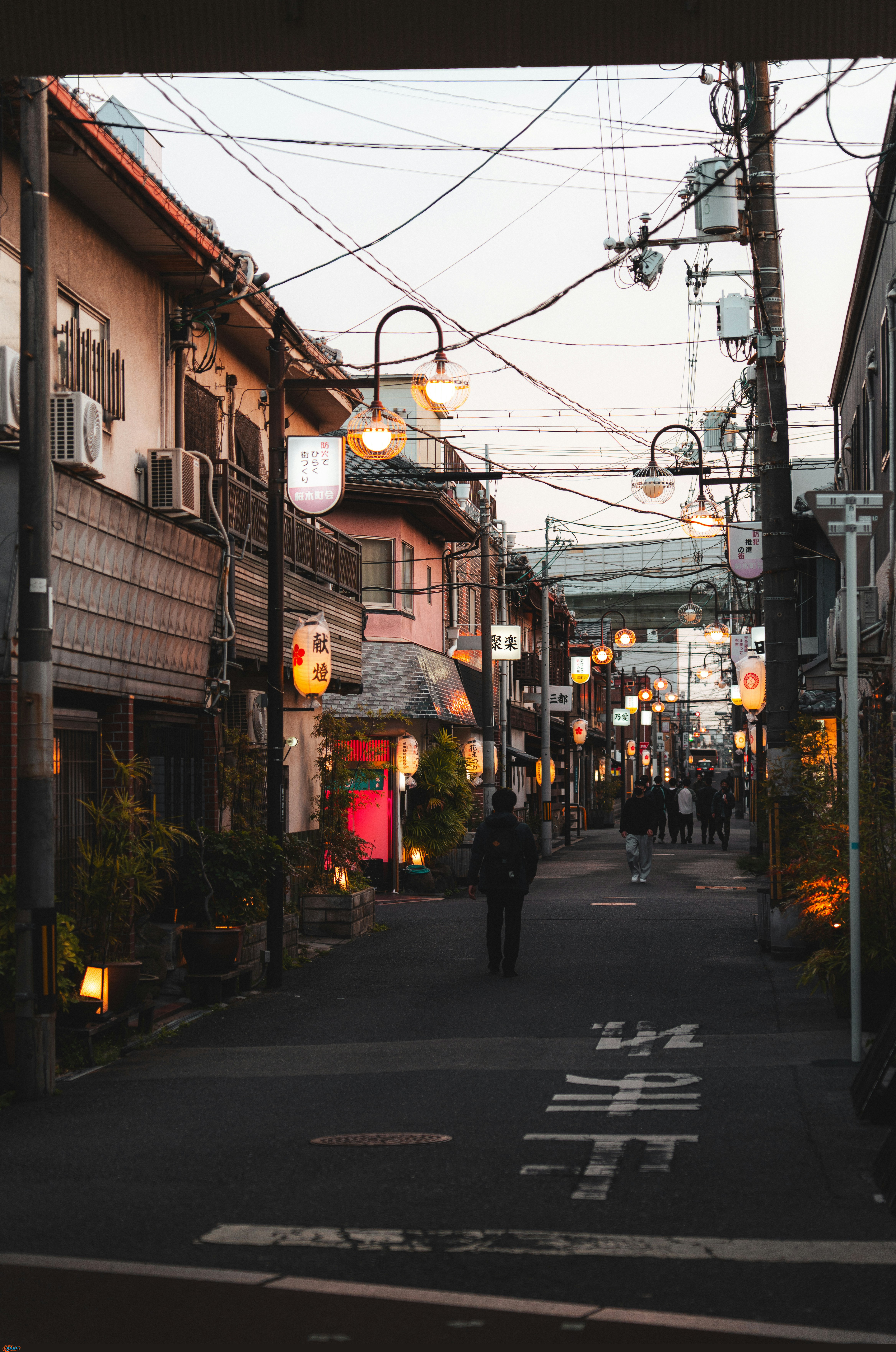 Urban street at dusk with people and illuminated lanterns by Alexander Kaufmann