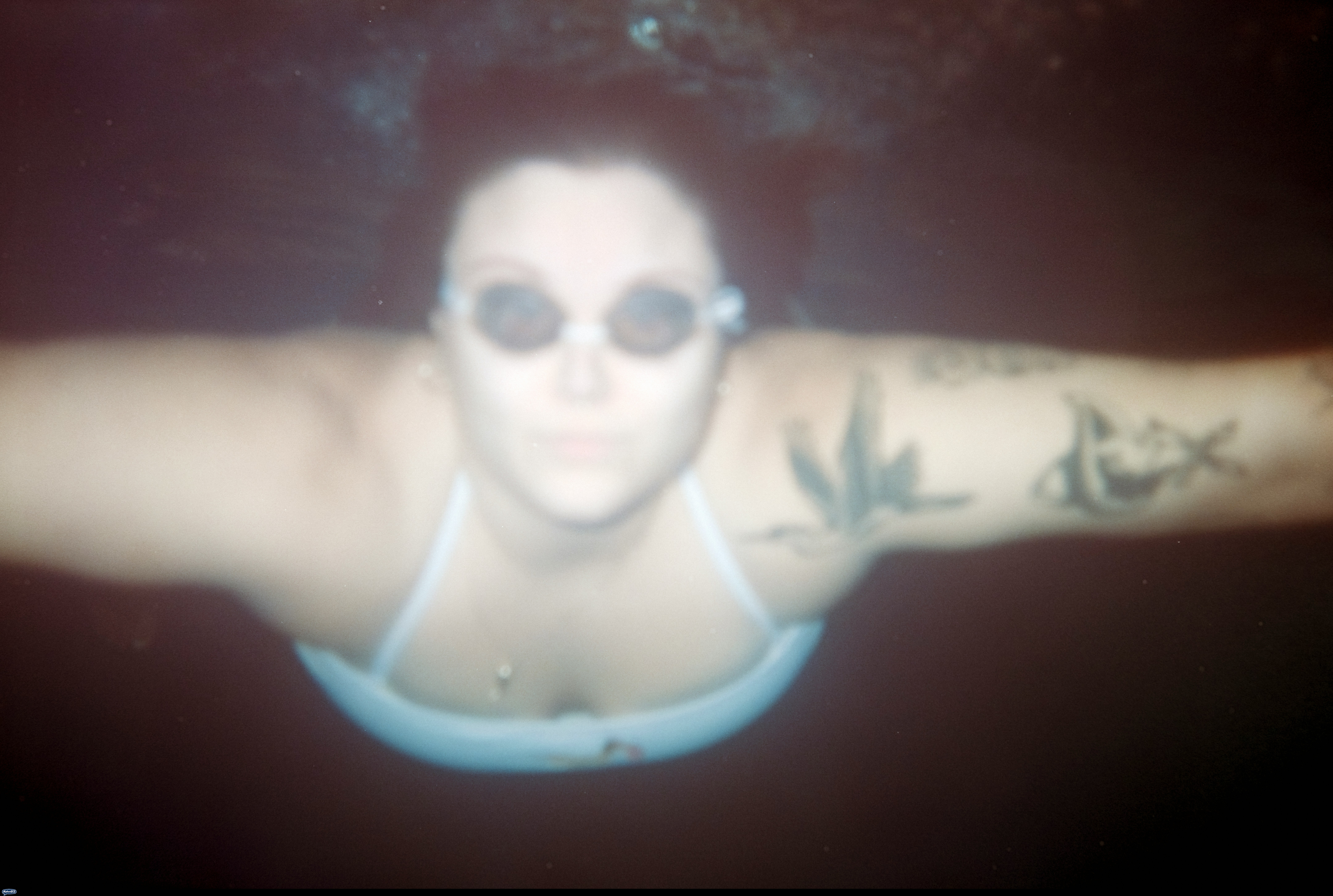 Woman swimming underwater in goggles with arm tattoos by Brooke Balentine
